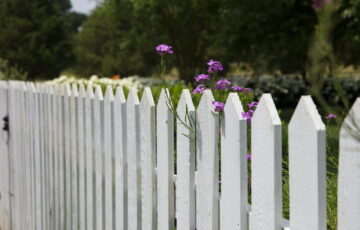Weißer Holzzaun mit lila Blumen – Tipps, um den Gartenzaun zu pflegen