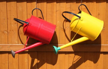 rote und gelbe Gießkanne am Zaun hängend